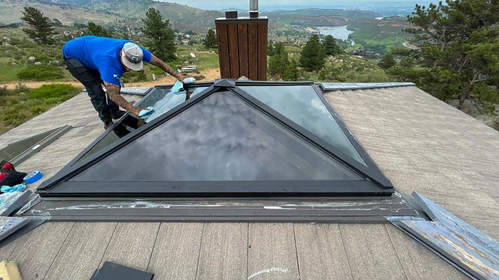 A skylight on a roof offers a view of distant mountains under a clear blue sky.