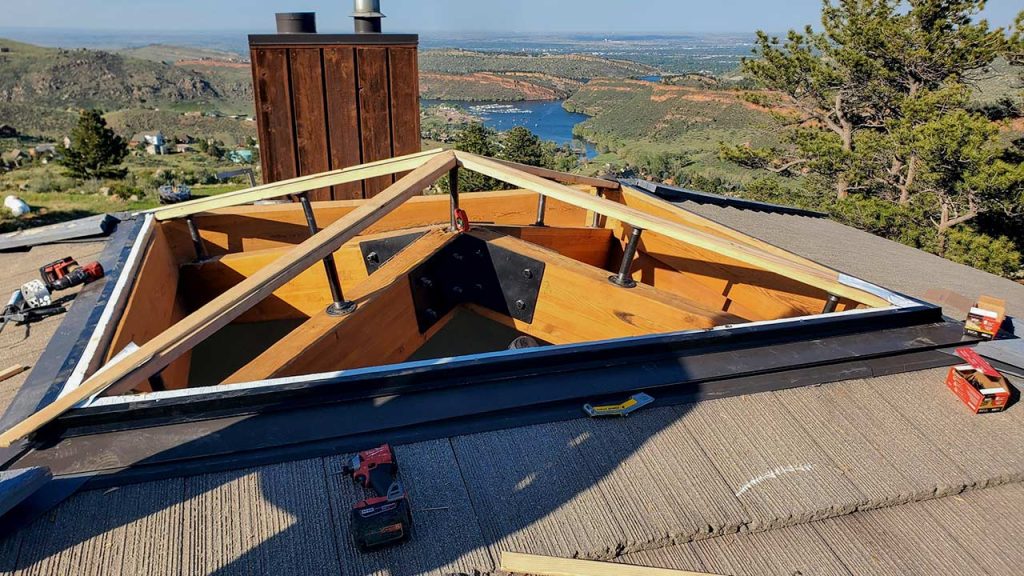 Rooftop construction scene with a pyramid wooden frame and tools scattered. Overlooks a lush landscape with hills, trees, and a serene lake.