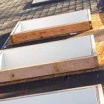 A technician on the roof installing underlayment around a skylight curb.