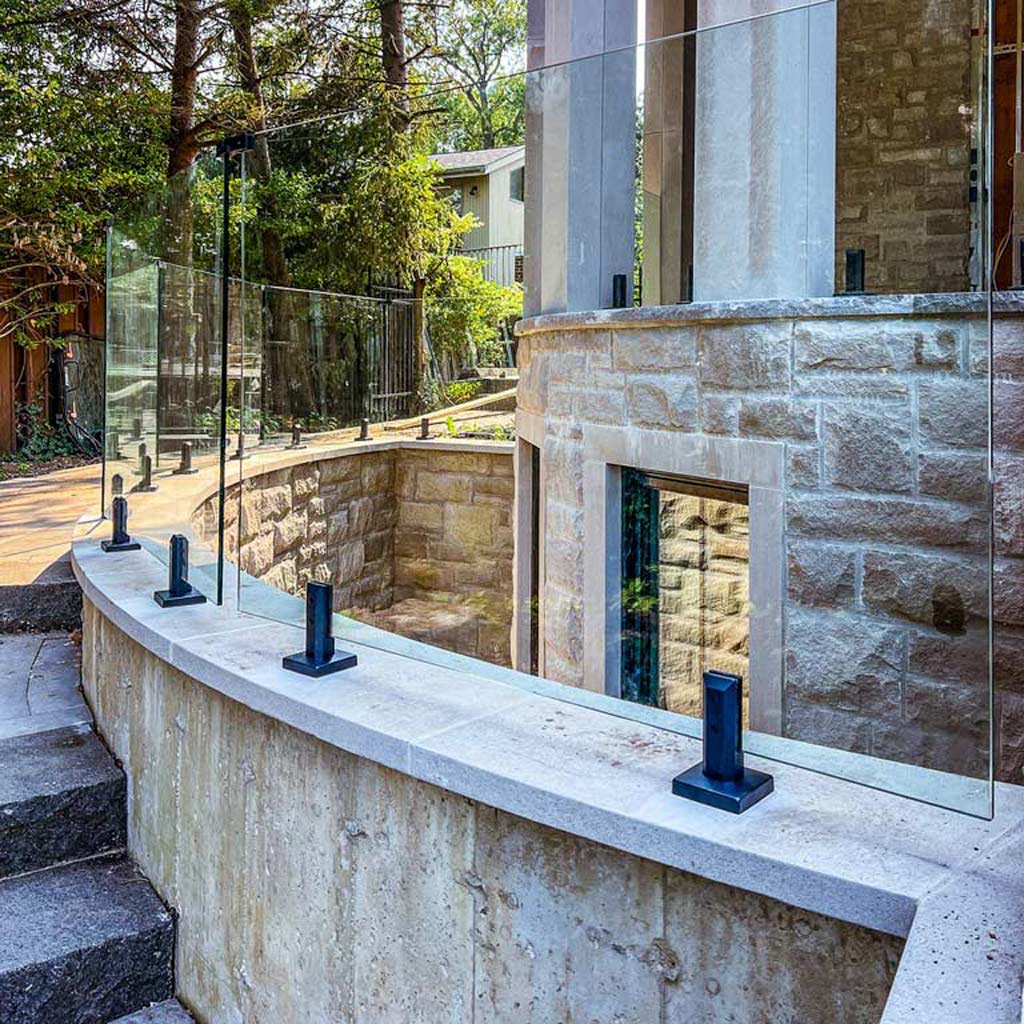 Modern architectural design featuring a curved concrete wall with a glass railing. Tall trees and a stone building create a serene, sophisticated atmosphere.