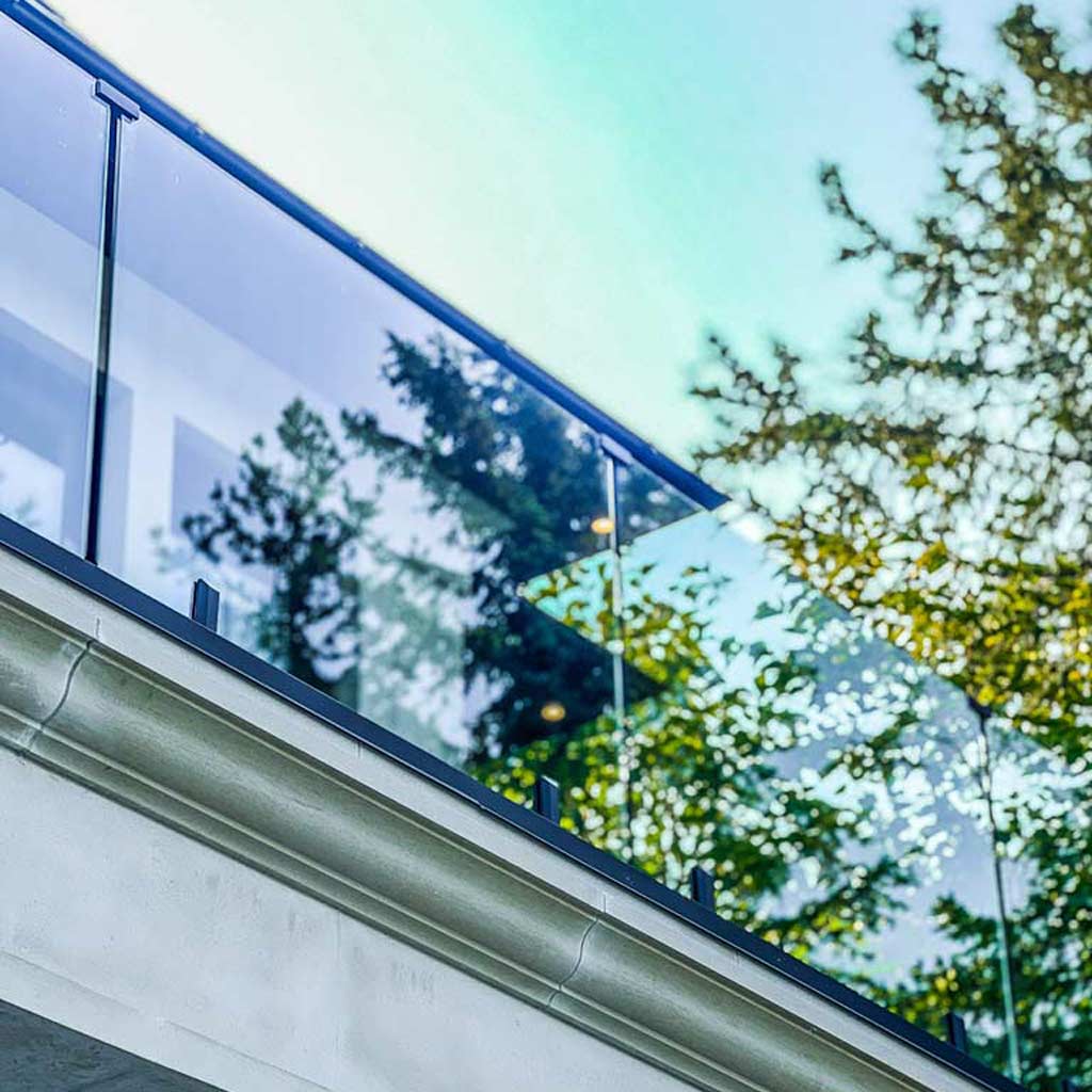 Modern glass railing with reflections of trees and sky, set against a clear blue backdrop. The scene conveys a sleek, serene architectural design.