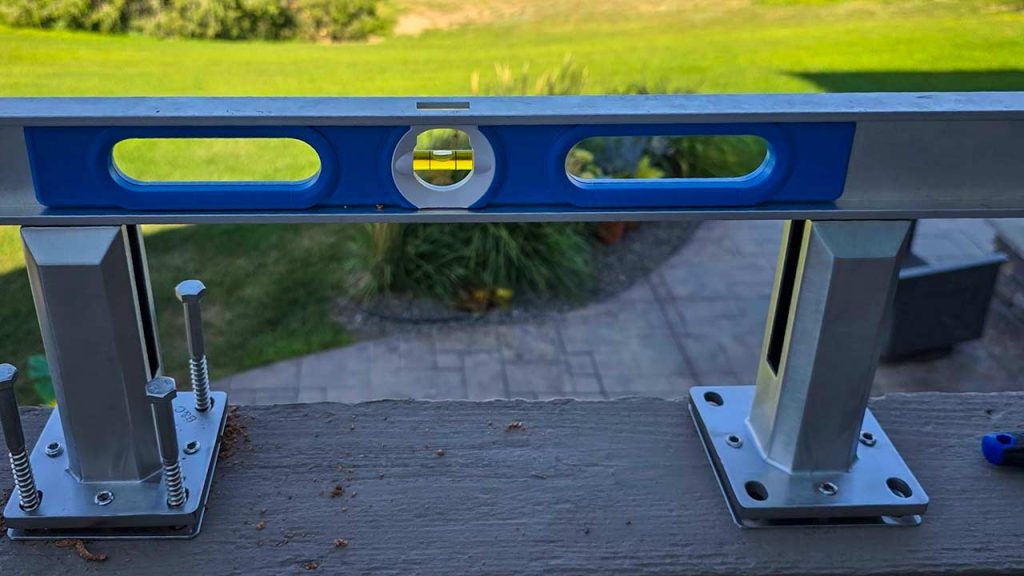A level tool placed on two metal brackets over a wooden deck, showing the bubble centered, against a background of a green lawn and patio.