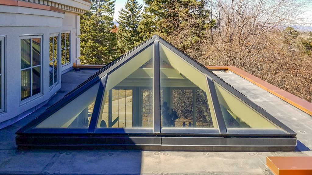 Rooftop exterior view of a glass extended pyramid skylight with dark metal framing installed on a flat roof.