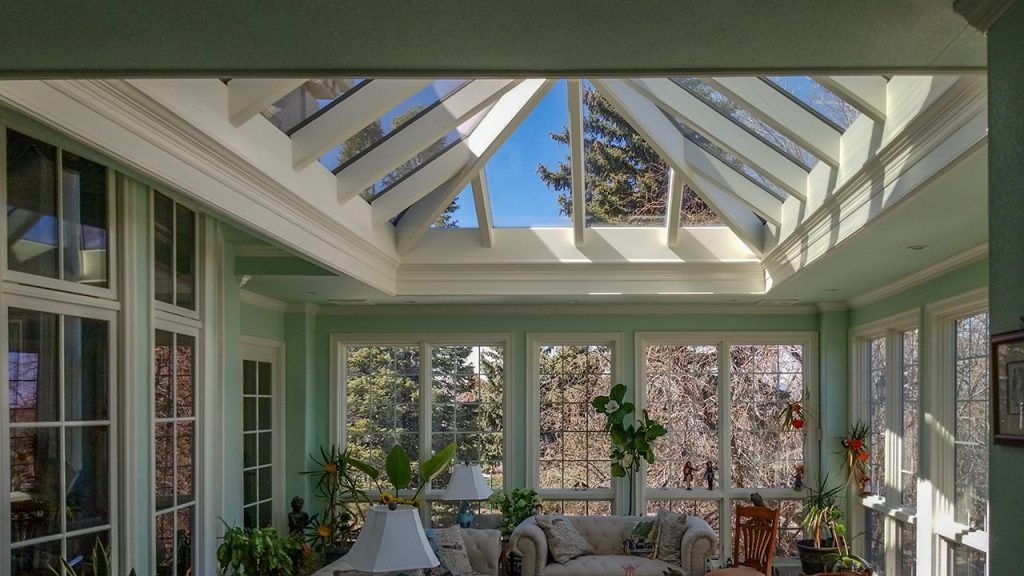 Interior view of a sunroom featuring an extended pyramid skylight and large glass windows overlooking greenery.