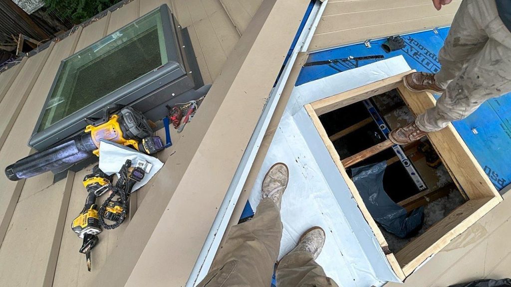 Rooftop view showing power tools and an open roof curb frame next to an installed VELUX VCM 3030 skylight.