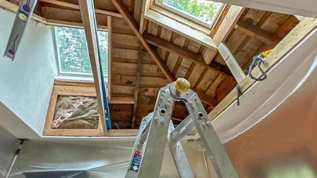 Ladder set up inside an open attic space under framed roof structure during VELUX FCM 3030 skylight installation.