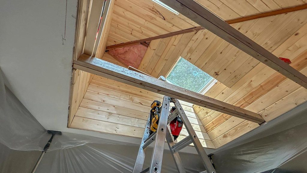 Interior view looking up through a wood-plank light shaft at a newly installed VELUX FCM 3030 skylight.