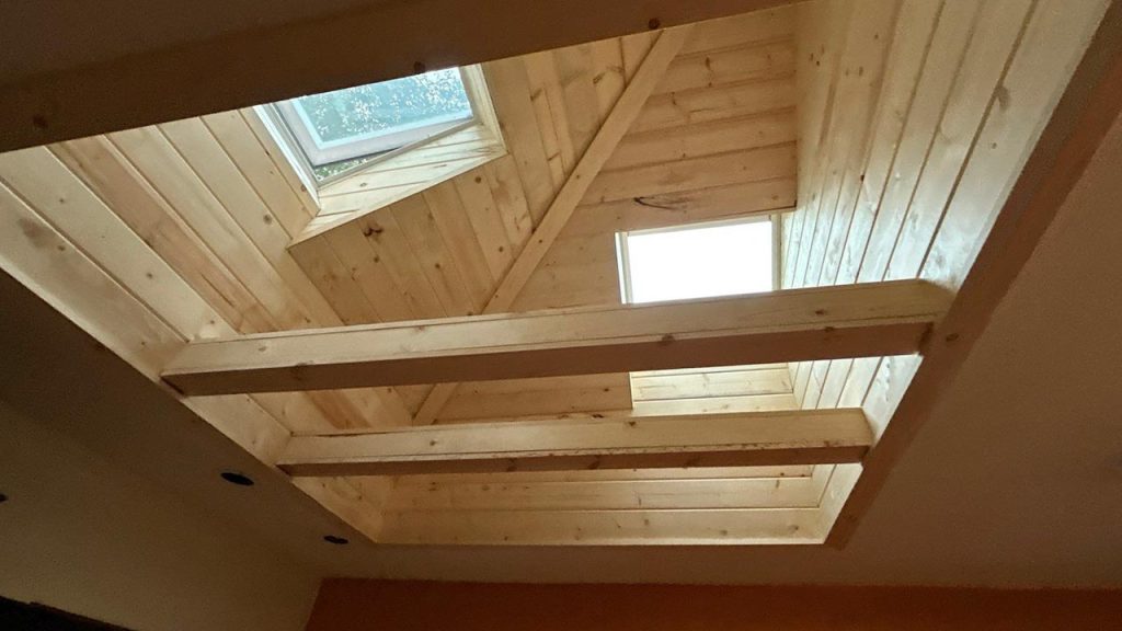 Finished tongue-and-groove wood ceiling shaft featuring double VELUX FCM 3030 skylights above exposed wooden beams.
