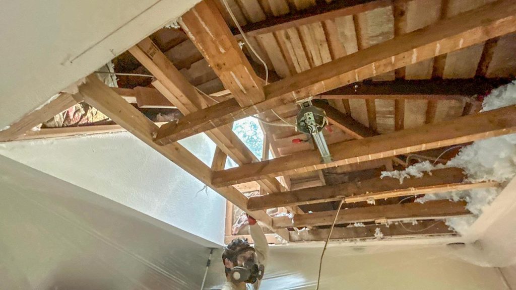 Installer wearing a respirator mask working on exposed attic framing beneath a VELUX FCM 3030 skylight opening.